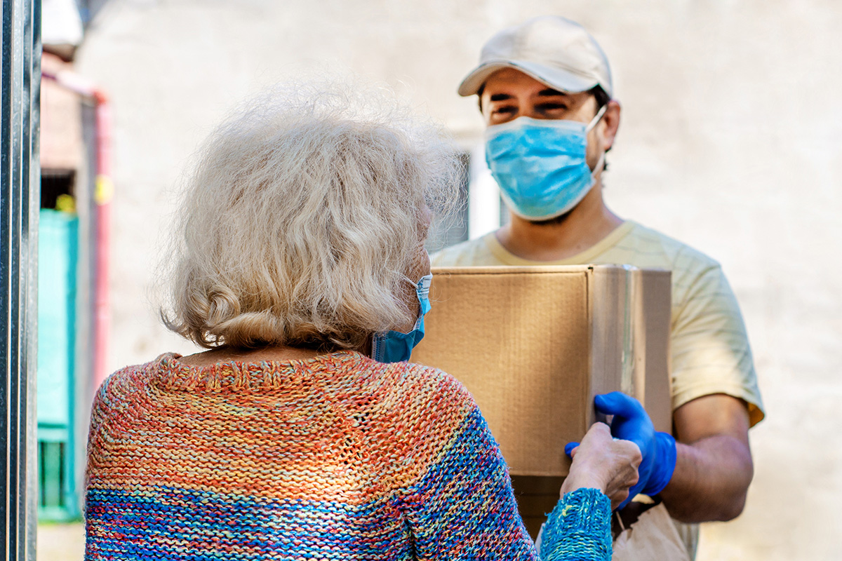 masked person handing a box to a senior lady